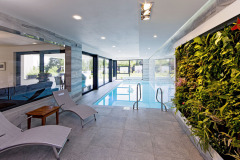 Bazén s prosklenými stěnami působí jako pokračování zahrady v interiéru. Kvetoucí zelená stěna sem přináší svěžest a živé barvy přírody