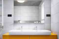Koupelna je opatřena velkoformátovým matným obkladem a černou dlažbou. Oranžový nábytek otepluje atmosféru