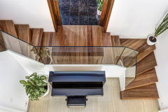 Otevřené schodiště je odděleno od zádveří dveřmi, které se zasouvají do stěny. Zábradlí z čirého kaleného skla umožňuje volný příčný průhled domem a odhaluje krásu tropického dřeva merbau na podestě a schodech
