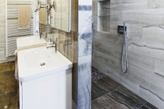 Koupelna v patře je  rozdělena příčkou na umyvadlovou část a sprchový kout, kde je dost místa pro sprchování ve dvou. Nábytková sestava byla vyrobena na míru, z lakovaných MDF desek, hladký bílý povrch krásně vynikne na pozadí italského obkladu a dlažby s výraznou kresbou mramoru