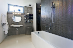 V koupelně se pohledový beton setkává s polyuretanovou stěrkou a mozaikou s metalickým efektem. Vedle umyvadla stojí betonová skruž – originální shoz na prádlo